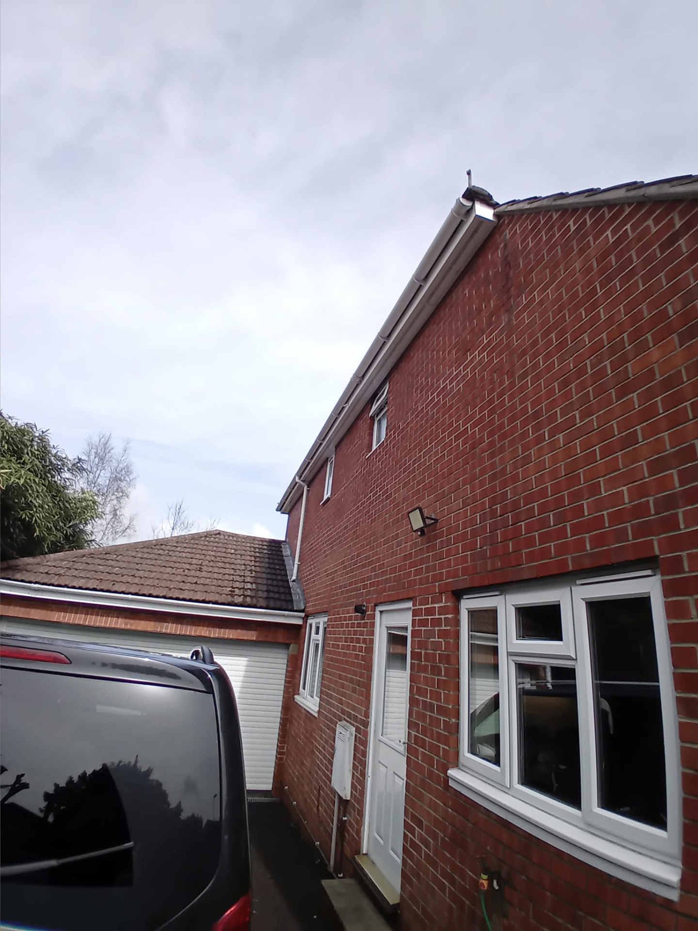 Clean white gutter line and fascia run along a red-brick side wall